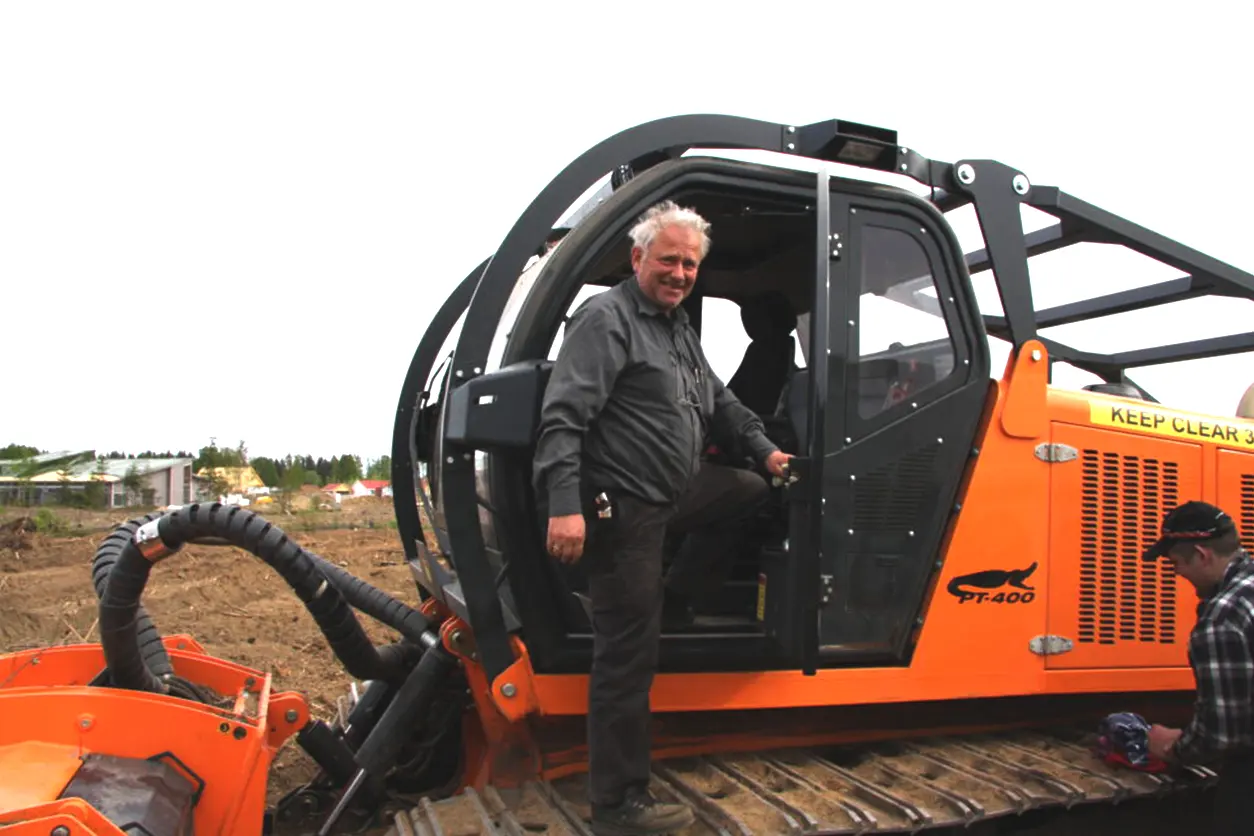 En mann som står i førerhuset på en oransje bulldoser og jobber med odel eller generasjonsskifte.