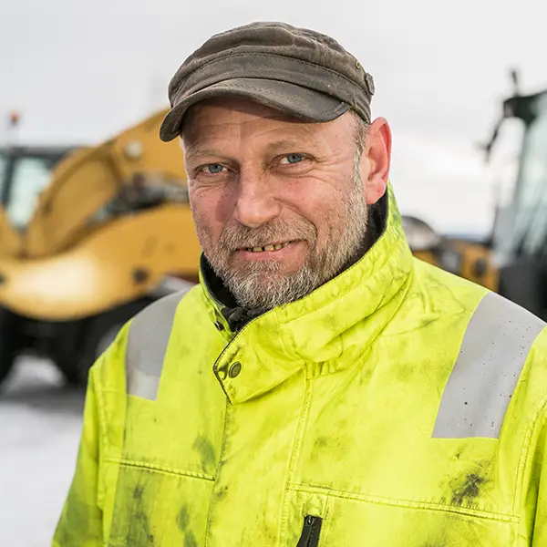 En mann i gul jakke som står foran en bulldoser på byggeplassen Kontakt REB Anlegg.