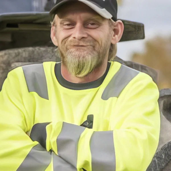 En smilende mann i gul skjorte poserer foran en bulldoser på byggeplassen Kontakt REB Anlegg.