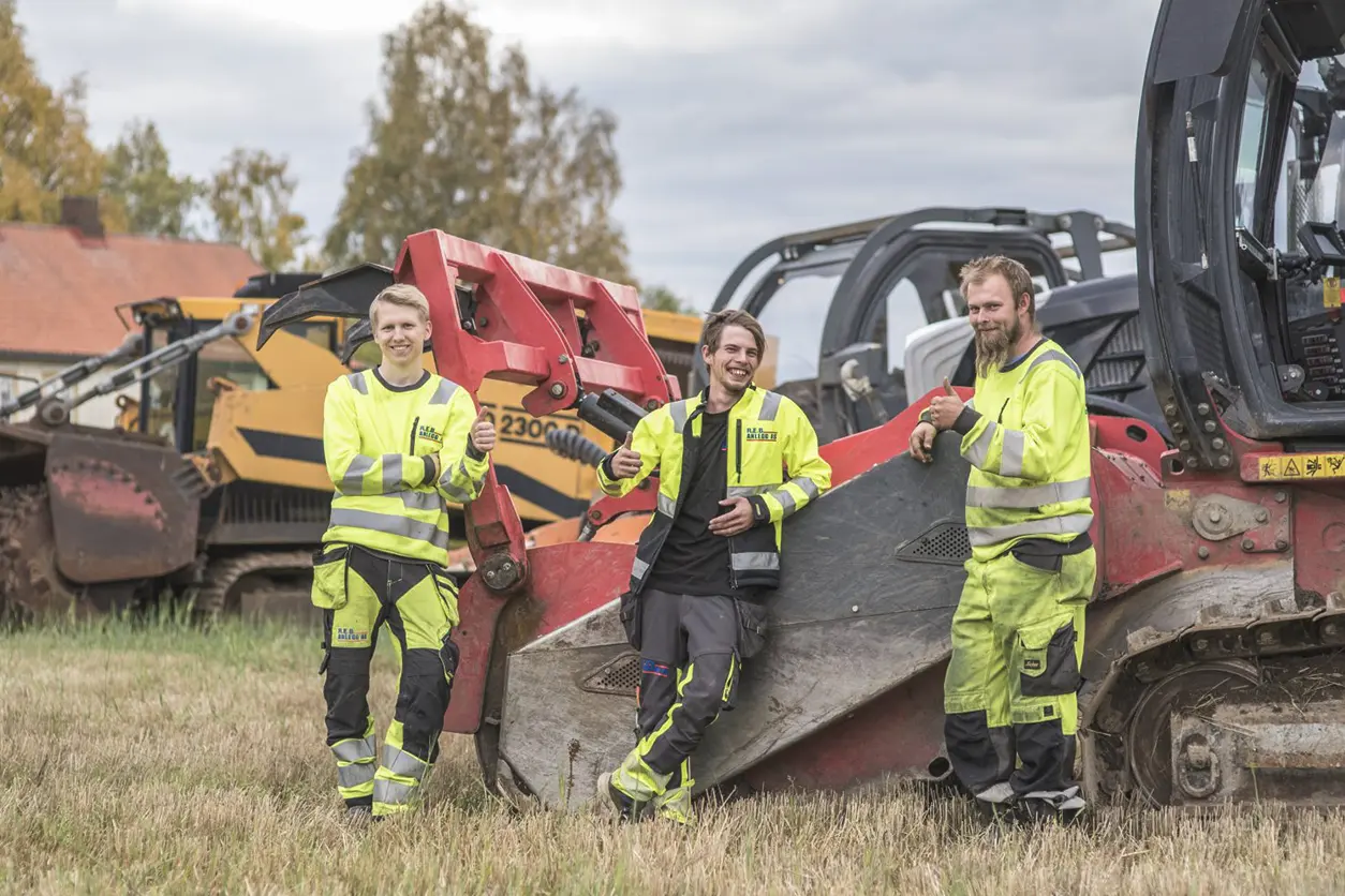 Tre menn står foran en bulldoser på en byggeplass.