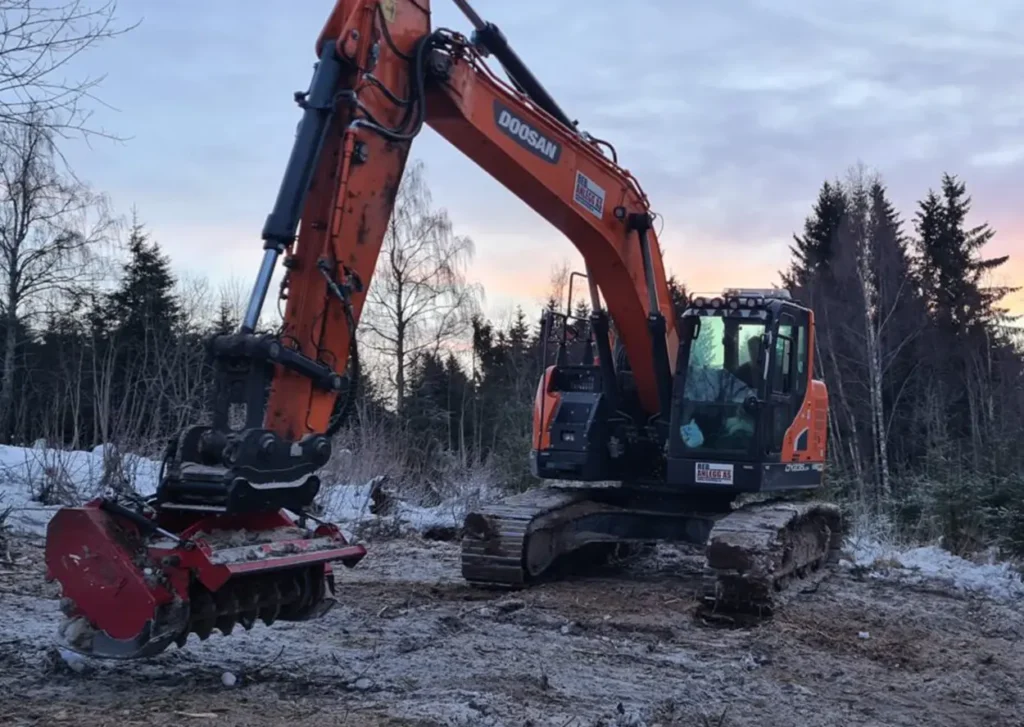 En reb orange gravemaskin sitter i snøen.