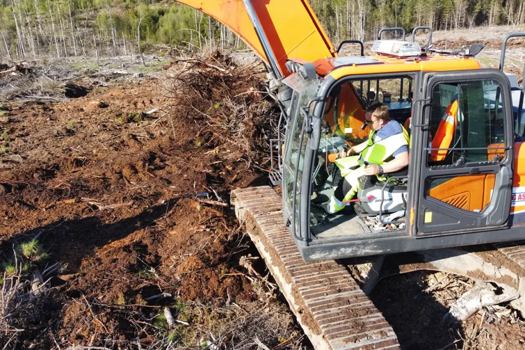 En mann som driver et anleggskjøretøy på en gård.