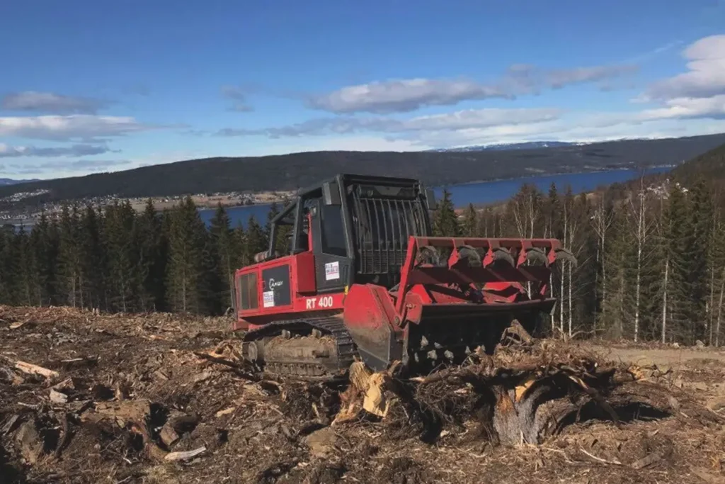 En Skanska rød bulldoser i skogen med en innsjø i bakgrunnen.