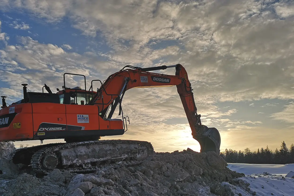 Skanskas oransje gravemaskin sitter på toppen av en steinrøys.