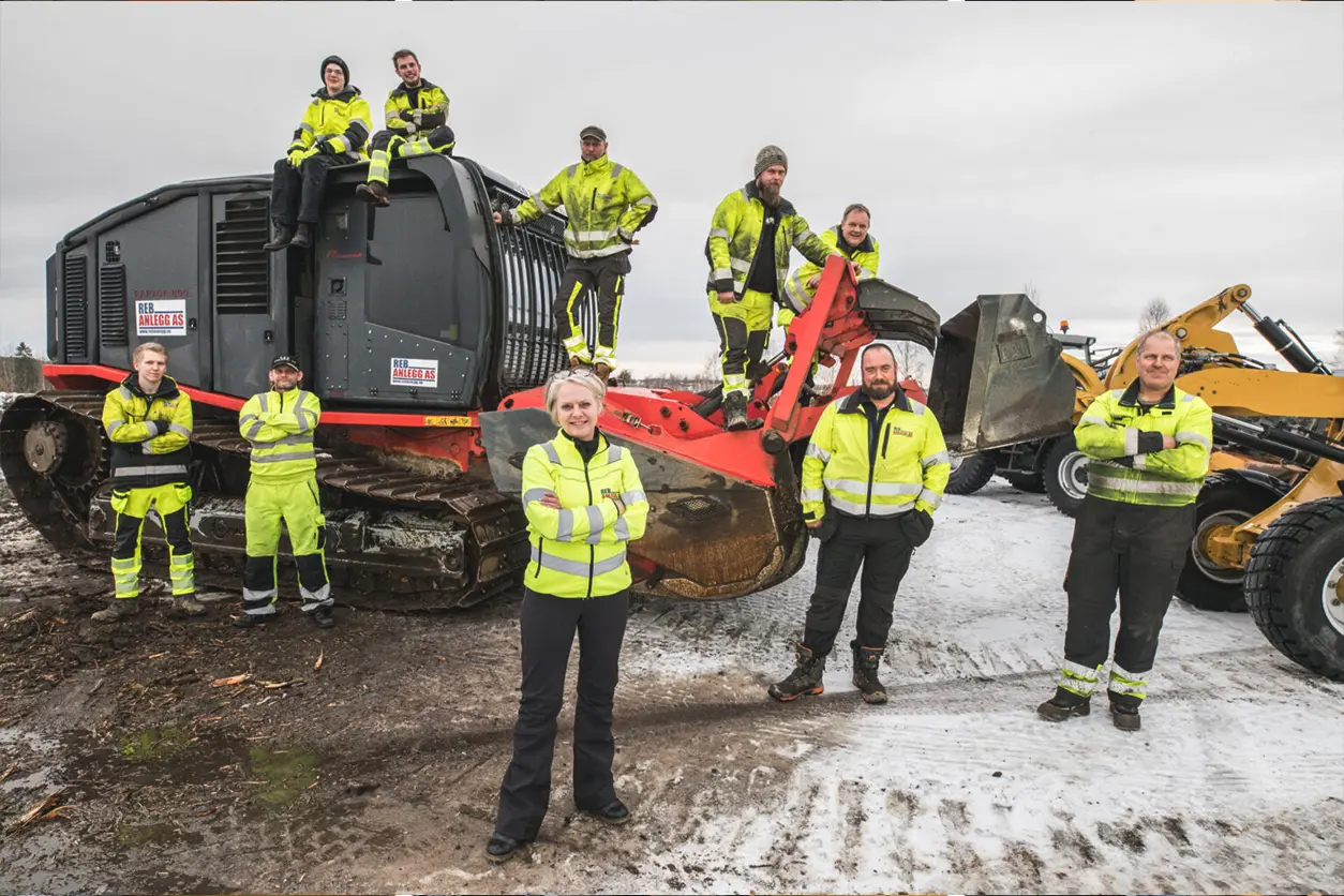 En gruppe bygningsarbeidere poserer foran en bulldoser, med en reb-maskin.