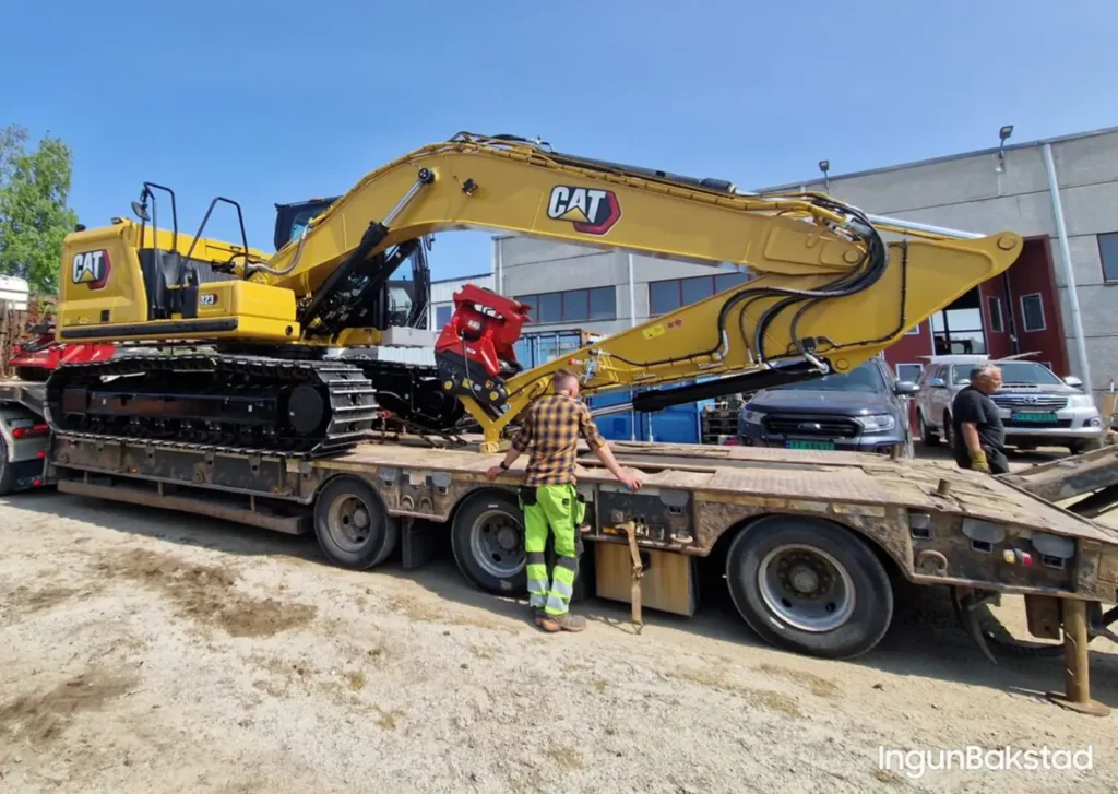 En ny CAT 323 gravemaskin blir lastet på en planbil.