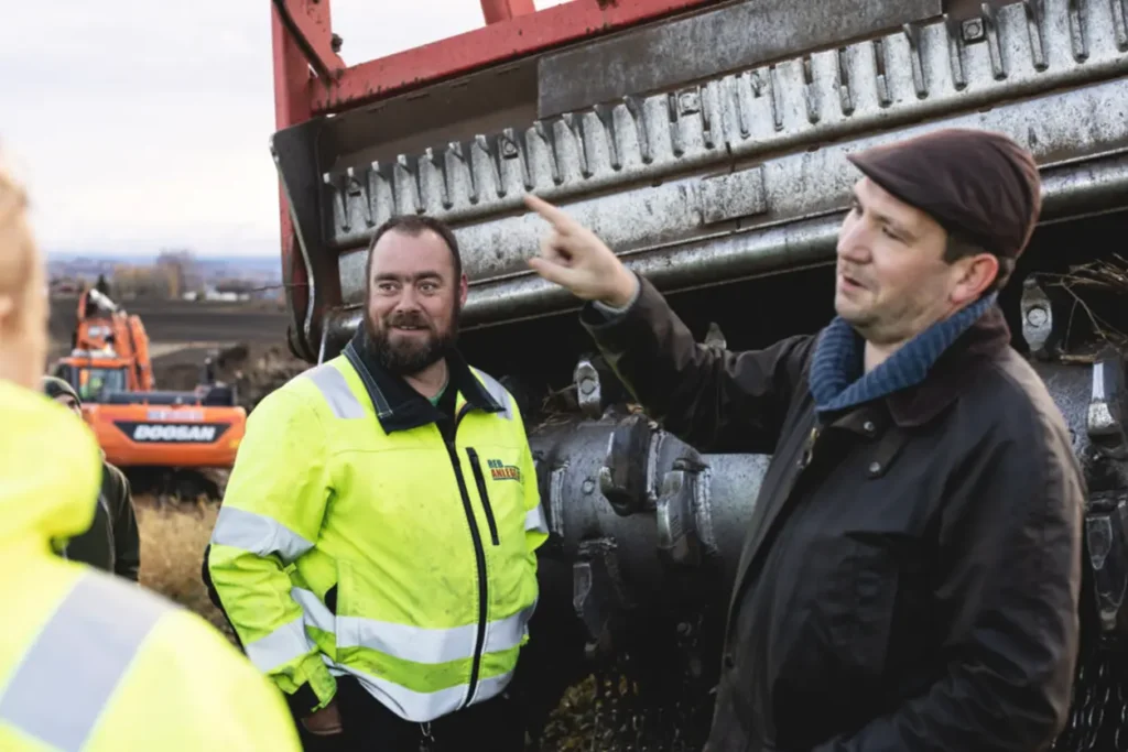 En gruppe menn som står ved siden av en stor traktor på en NRK byggeplass.