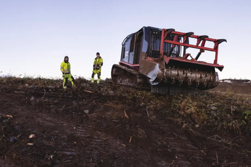 To menn som står ved siden av en bulldoser på en høyde under et byggeprosjekt.